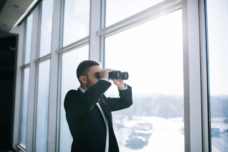 Businessman looking out the window with binoculars