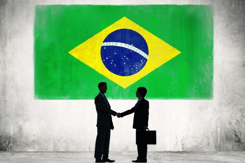 Businessmen shaking hands in front of Brazilian flag