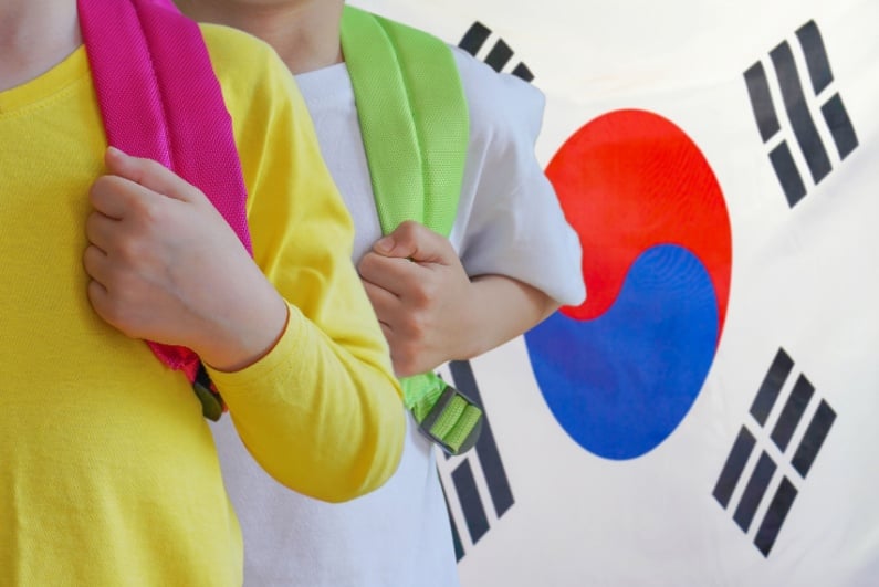 Two children with backpacks in front of South Korean flag