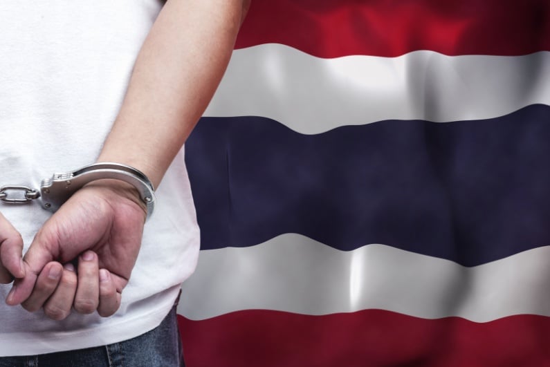 Handcuffed person in front of Thai flag