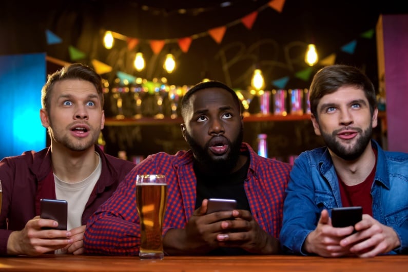 Men clutching their phones watching sports at a bar