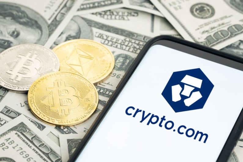 Crypto.com logo on phone with cash and representations of physical cryptocurrency